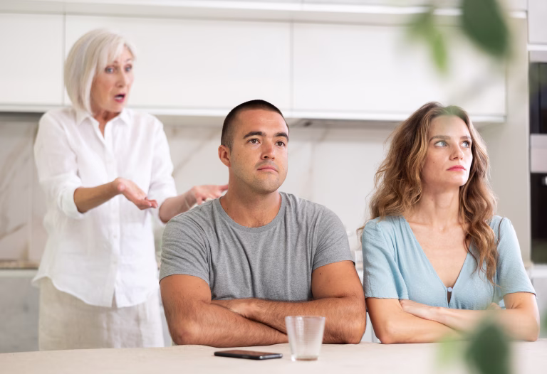 Young couple quarrel with mother while sitting at table in kitchen