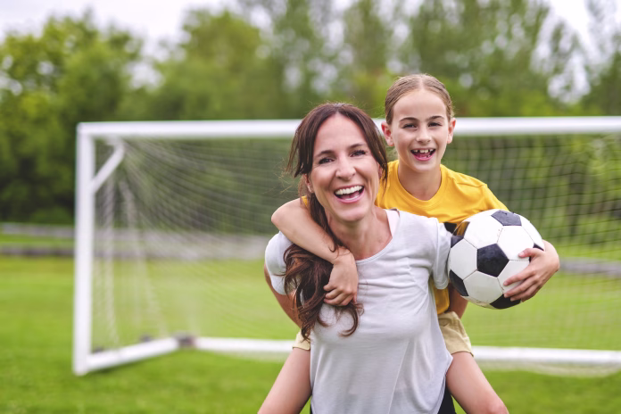 A happy mother playing football outdoor on a summer day with her daughter