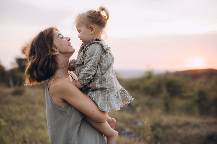 A joyful mother holding her daughter outdoors during a stunning sunset, symbolizing love, family bonds, and warm emotions in a serene nature setting.