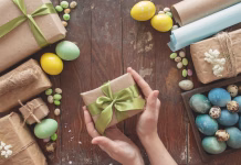 6 idej za velikonočna darila, ki niso čokolada A young woman holds a gift in her hands. Colored eggs and holiday symbols on a dark wooden table. Zero waste concept.