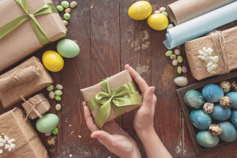A young woman holds a gift in her hands. Colored eggs and holiday symbols on a dark wooden table. Zero waste concept.