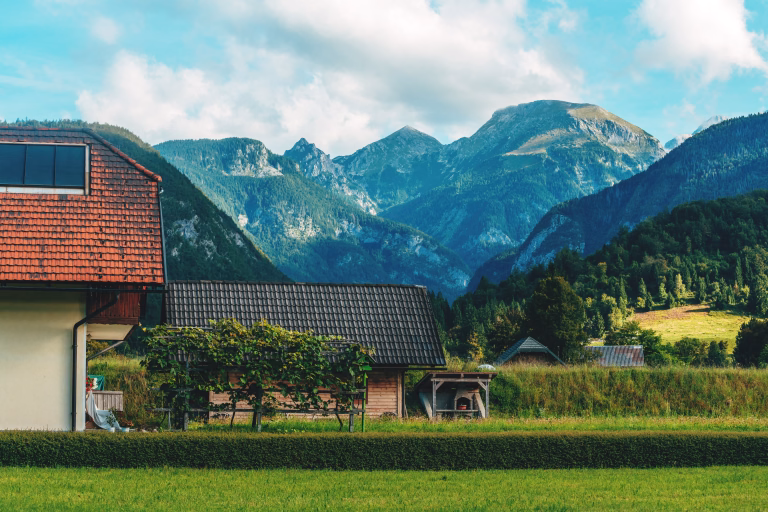Beautiful alpine house with farmland backyard in Bohinj valley, Julian Alps mountains in the background on a bright summer morning. Selective focus.
