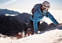 Kako preprečiti višinsko bolezen na trekingu ali alpinistični odpravi? Climber in a blue jacket and helmet ascends a snowy peak, flanked by two companions, symbolizing teamwork and adventure in a breathtaking mountain landscape.