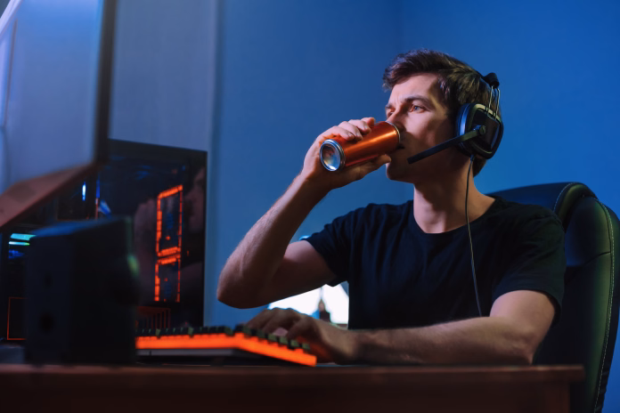 Cyber sport. Professional cybersport player training or playing online video game on his PC late at night, drinking caffeine energy drink to concentrate, focus on game. Team play. Games addiction