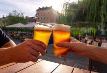 To so najboljše pivovarne v Sloveniji za leto 2026: deseterica, ki je navdušila friends cheers toast with two beers in summer sunshine in Ljubljana outdoor pub .