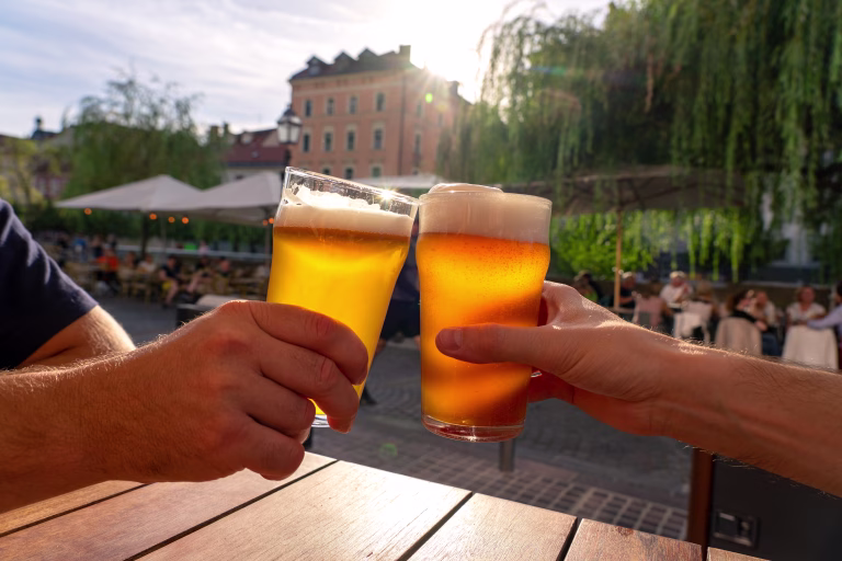 friends cheers toast with two beers in summer sunshine in Ljubljana outdoor pub .