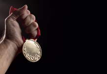 Katera država je plačala največ za zlato olimpijsko medaljo? hand holding a gold medal on black with blank face for text, concept for winning or success