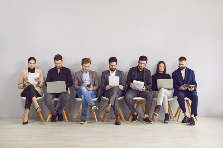 Happy young professional business people, group of applicants are sitting on chairs, waiting for interview, sitting in line with laptops, notebooks and other resources. Staffing employment concept.