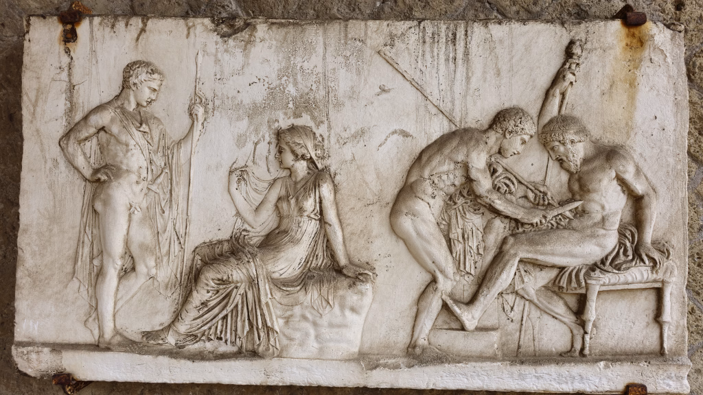 Herculaneum, Italy - 9 January 2025. In the House of the Relief of Telephus, a carved marble panel shows a mythological scene with four figures, including a warrior being tended to.