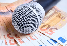 Objavljena štipendija za petje mladih slovenskega rodu Microphone over euro bills background close up shot. Microphone lies on scattered euro banknotes. Concept of karaoke club, artist fee, payment for performance, professional musicians career.