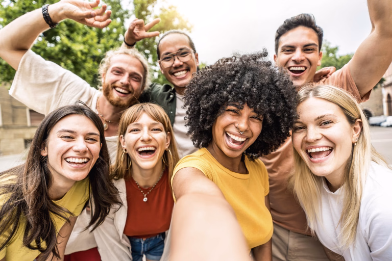 Multicultural friends smiling at camera together outside - Happy young people taking selfie with smart mobile phone device walking on city street - Youth community and technology concept