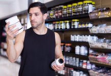 L-glutamin ali kreatin: Kaj je bolje za regeneracijo mišic? Serious muscular guy holding sport nutrition products in sport shop