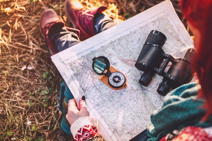 Traveler young woman searching direction with a compass on background of map in the forest