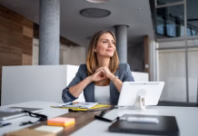 Strokovnjaki menijo, da se tej plati življenja na posveča dovolj pozornosti: Ste vi pozorni na ta del kariernega razvoja? Businesswoman sitting at a modern office desk, smiling and gazing thoughtfully into the distance while contemplating future business plans and aspirations for success