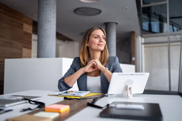 businesswoman-sitting-at-a-modern-office-desk-smiling-and-gazing-thoughtfully-into-the-distance-while-contemplating-future-business-plans-and-aspirations-for-success-stockpack-istock Businesswoman sitting at a modern office desk, smiling and gazing thoughtfully into the distance while contemplating future business plans and aspirations for success