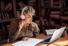 Glasba tega skladatelja je najboljša za učenje Concentrated and focused young adult woman sitting behind desk with laptop in library, study at university. Student girl writing exercise task and listening music in headset