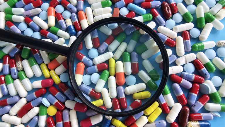 Many colorful pills and capsules spread across a surface with a magnifying glass on them