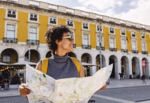 Kako potovati bolj trajnostno? Smiling tourist is holding a map and wearing a yellow backpack while visiting the beautiful city of lisbon in portugal during summer vacations