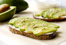 Pozabite trendovski avokado: teh 6 živil vsebuje več zdravih maščob Vegan sandwich, rye bread toast, avocado slices, vegenaise sauce & raw arugula. Toasted sourdough, eggless mayonnaise, wooden table, whole & halved. National avocado day concept. Close up, background.