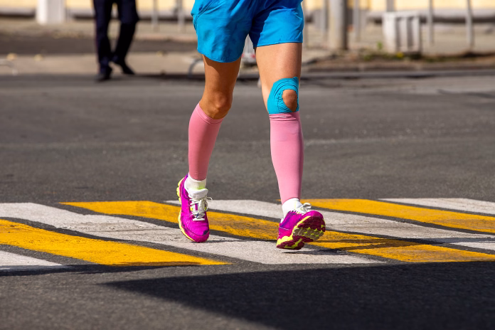 woman-runner-legs-in-pink-compression-sleeves-and-knee-in-kinesiotape-stockpack-istock Woman runner legs in pink compression sleeves and knee in kinesiotape