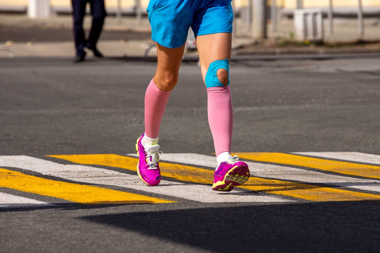 Woman runner legs in pink compression sleeves and knee in kinesiotape