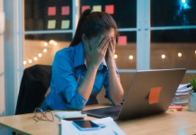 Ko ne pomaga nobena strategija in ni krivo pomanjkanje discipline: morda je to vzrok za pomanjkanje koncentracije Working late into the night, Asian woman appears stressed and overwhelmed at her desk, rubbing her forehead as if experiencing migraine or headache, surrounded by paperwork and dimly lit office.