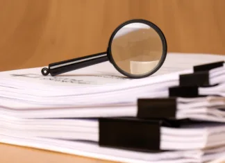 Po 100 letih razvozlali Schrödingerjevo skrivnost A magnifying glass rests on scattered clipped papers, symbolizing diligent research and careful analysis