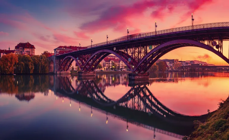 Beautiful view of Maribor city, Slovenia, at sunrise, with river, bridge and dramatic sky. Travel outdoor landscape.