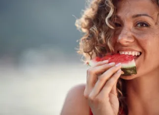 5 živil, ki odlično hidrirajo telo: obvezno jih jejte med hudo vročino Beautiful young woman with curly hair biting on watermelon piece. Summertime, lifestyle concept.