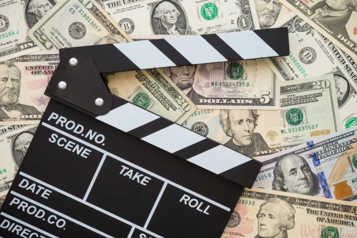 Cinema clapperboard on stack US dollars banknote bill background - Movie entertainment industry to make money concept.