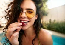 Nosite sončna očala? Strokovnjaki pravijo, da bi jih morali veliko pogosteje Close-up of a beautiful young woman in sunglasses about to eat a raspberry. Outdoor summer scene with pool in background. Healthy lifestyle and freshness.