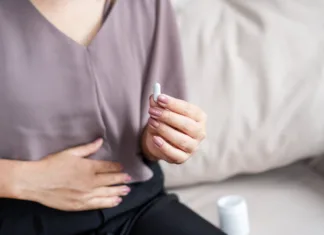 Veliko ljudi jemlje probiotike napačno: Ali jih tudi vi? Close-up of a woman’s hand holding a white pill, taking medicine to help relieve stomach pain or digestive problems like IBS, constipation, or diarrhea, aiming to improve her comfort