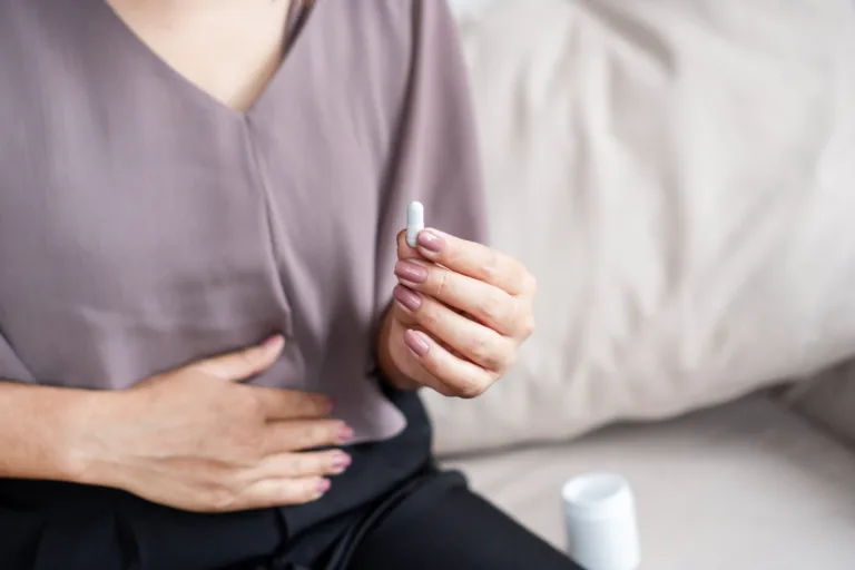 Close-up of a woman’s hand holding a white pill, taking medicine to help relieve stomach pain or digestive problems like IBS, constipation, or diarrhea, aiming to improve her comfort
