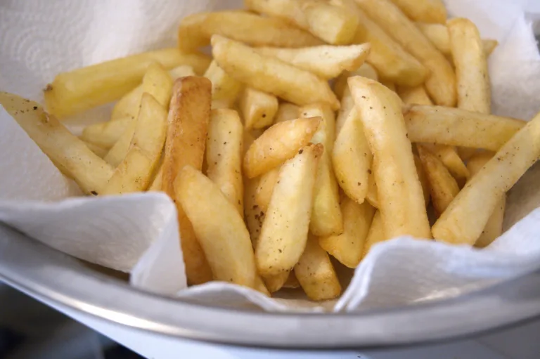 Close-up of freshly fried french fries resting on paper towel showing oil absorption, unhealthy eating habits and everyday lifestyle choices in natural condition with Copy Space.