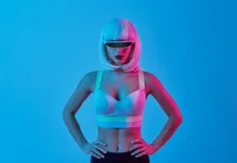Ali lahko prepoznate AI vplivneža? Ne obstajajo, a imajo na tisoče sledilcev Futuristic female cyborg in digital glasses and bra keeping hands on waist and looking at camera against blue background