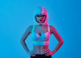 Ali lahko prepoznate AI vplivneža? Ne obstajajo, a imajo na tisoče sledilcev Futuristic female cyborg in digital glasses and bra keeping hands on waist and looking at camera against blue background
