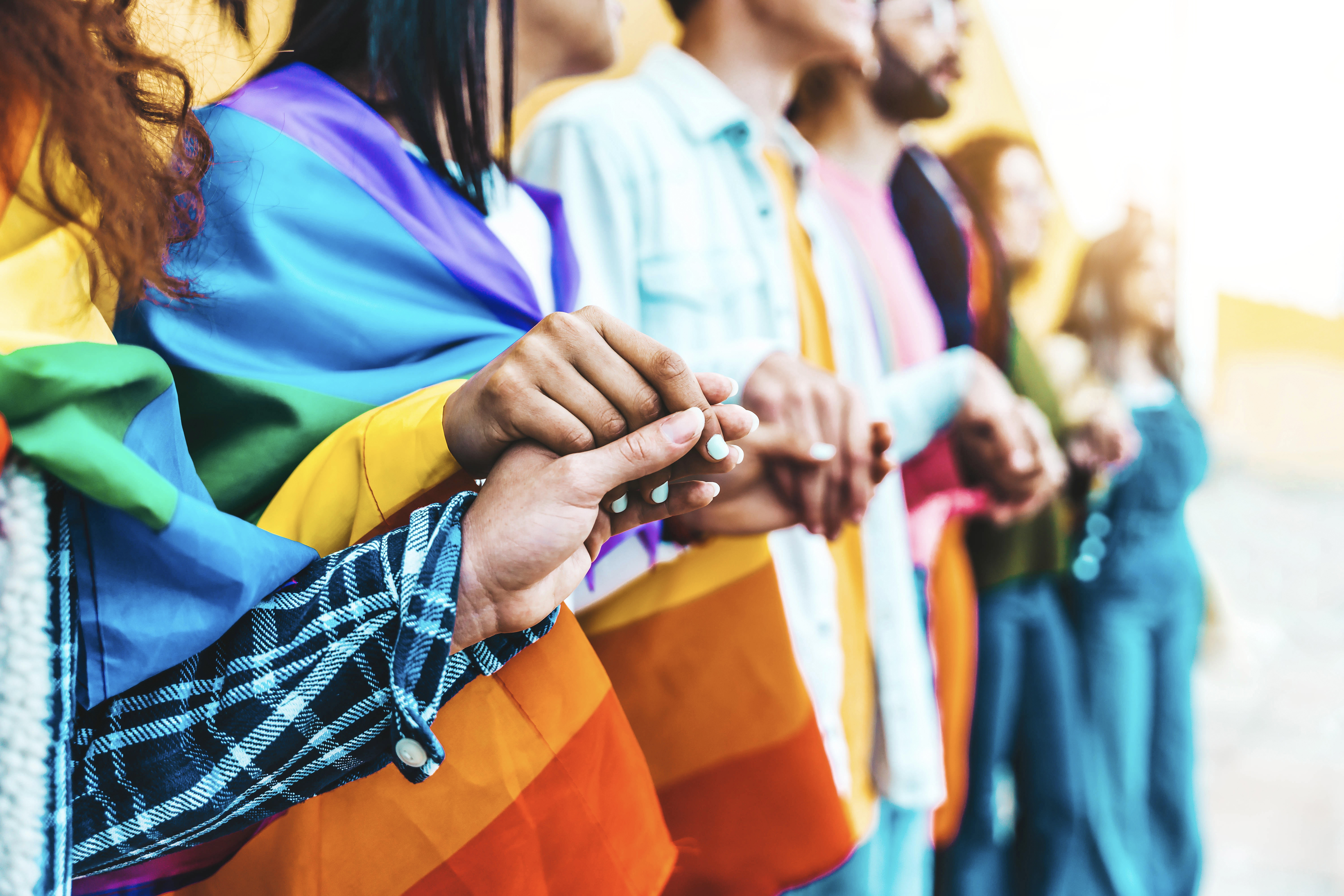 Group of lgbt people holding hands outside - Diverse happy friends hugging outdoors - Gay pride concept with crowd of guys and girls standing together on city street
