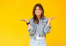 Nič me ne zanima: Kako ugotoviti, kaj bi počeli v življenju? I don't know. Portrait of confused beautiful brunette young woman with makeup in denim casual style standing with raised arms, looking away and doubt. indoor studio shot, isolated on yellow background