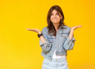 Nič me ne zanima: Kako ugotoviti, kaj bi počeli v življenju? I don't know. Portrait of confused beautiful brunette young woman with makeup in denim casual style standing with raised arms, looking away and doubt. indoor studio shot, isolated on yellow background