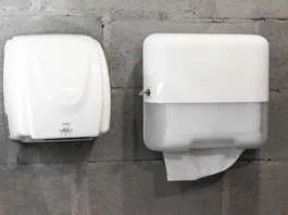 Večina ljudi ne ve, kaj je bolj higienično: Bi izbrali papirnate brisače ali sušilnik? Paper towel dispenser and hand dryer on concrete wall on modern stylish bathroom in loft style