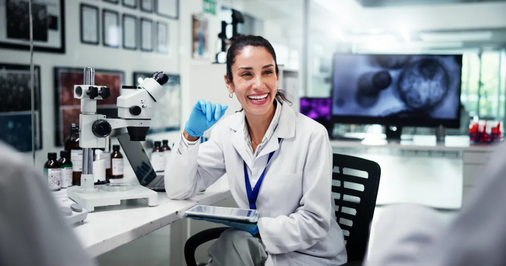 Research, smile and woman with tablet, science and meeting for experiment results. Healthcare, employees or scientists in laboratory, tech or digital app for vaccine development, planning or feedback