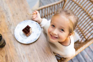 Smiling young girl sitting at an outdoor cafe table with a dessert. Joyful moment and outdoor dining
