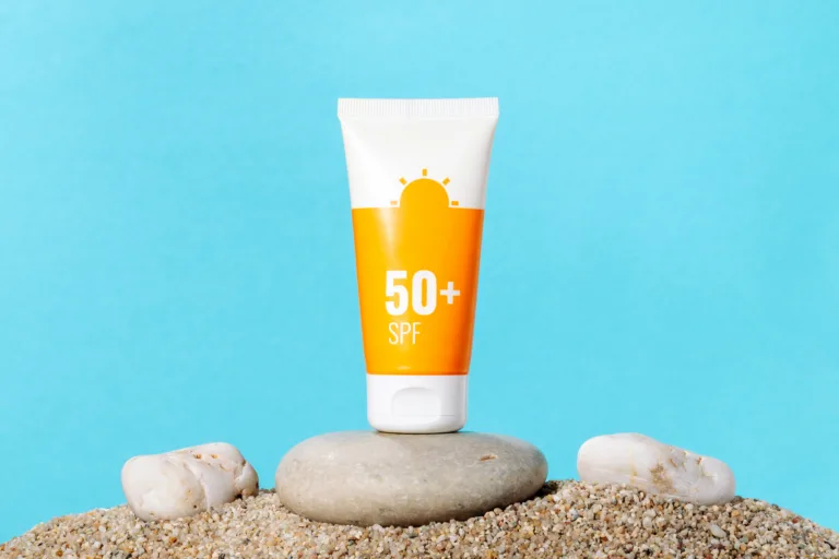 Sunscreen in an orange tube on blue background with beach sand, copy space. Summer beach, vacation concept, spf uv-protect cosmetics