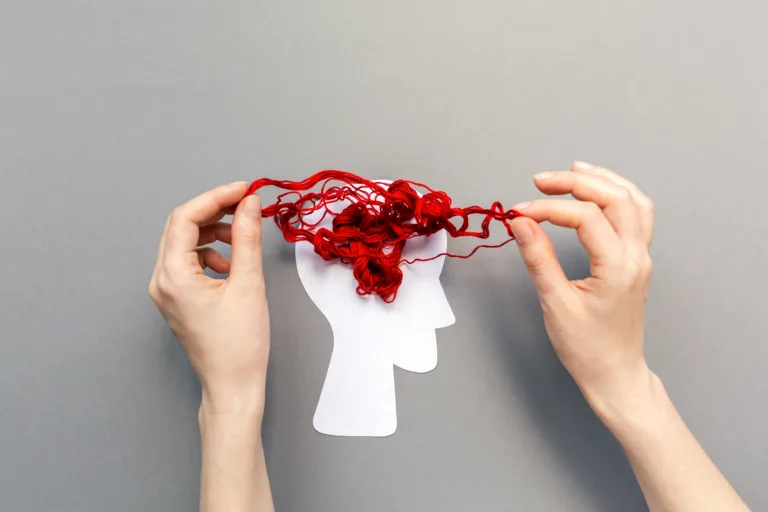Tangled red threads on the silhouette of the head, representing the brain. Blue background. Flat lay. The concept of mental health and demension