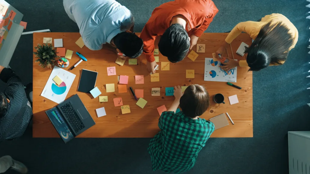 Top down aerial view of business team brainstorming idea and writing plan at colorful sticky notes. Professional project manager planning strategy while stick paper at meeting table. Convocation.