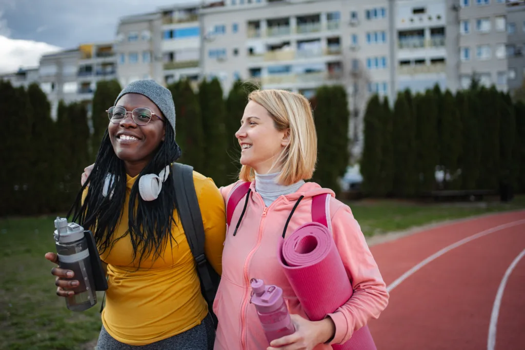 Two happy young adult women friends walking on a running track with fitness gear