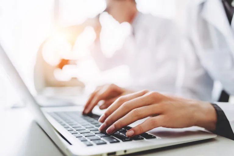 Two scientists are working in laboratory. Cropped image of young female researcher and her senior supervisor are doing investigations with microscope and laptop.
