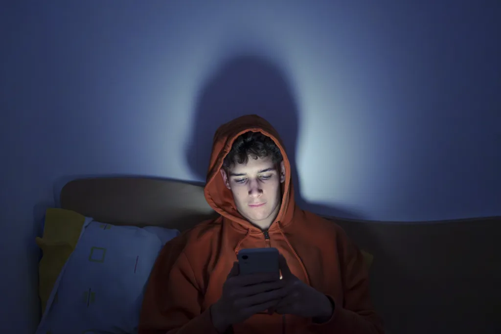Young man using mobile phone late at night in his bedroom