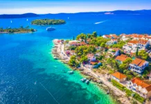 5 najlepših plaž na Hrvaškem v letu 2026 A beautiful aerial view of the Mediterranean landscape surrounding Maslinica on Solta Island, Croatia, featuring pine forests, traditional stone houses, and the deep blue Adriatic Sea