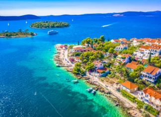 5 najlepših plaž na Hrvaškem v letu 2026 A beautiful aerial view of the Mediterranean landscape surrounding Maslinica on Solta Island, Croatia, featuring pine forests, traditional stone houses, and the deep blue Adriatic Sea